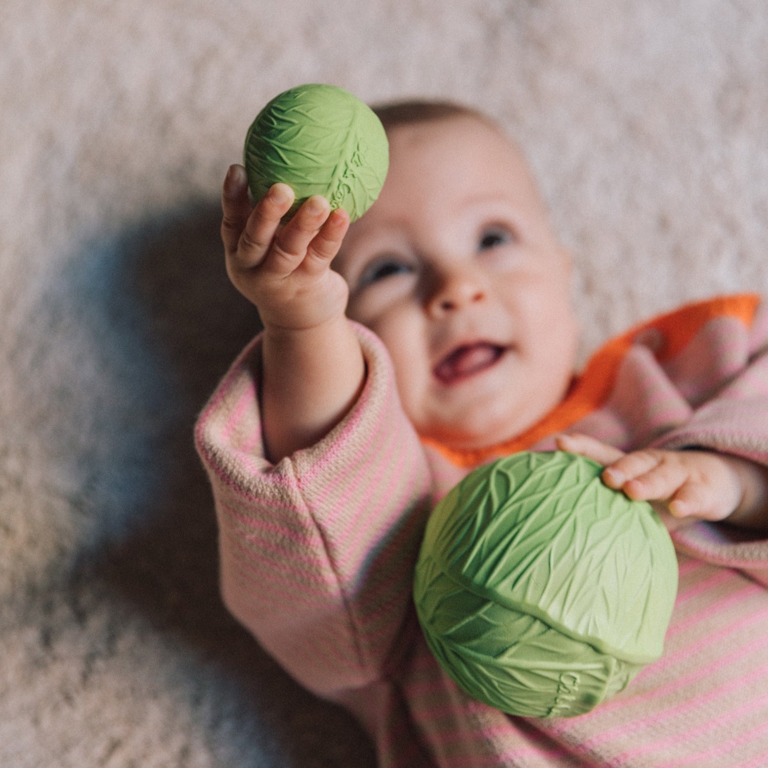 Baby holding green cabbage-shaped toys on a carpeted floor