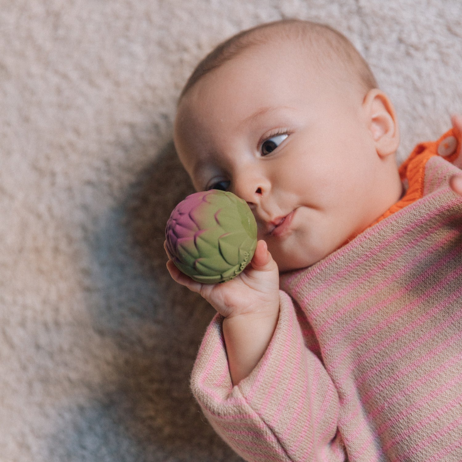 Baby holding a colorful ball on a soft surface