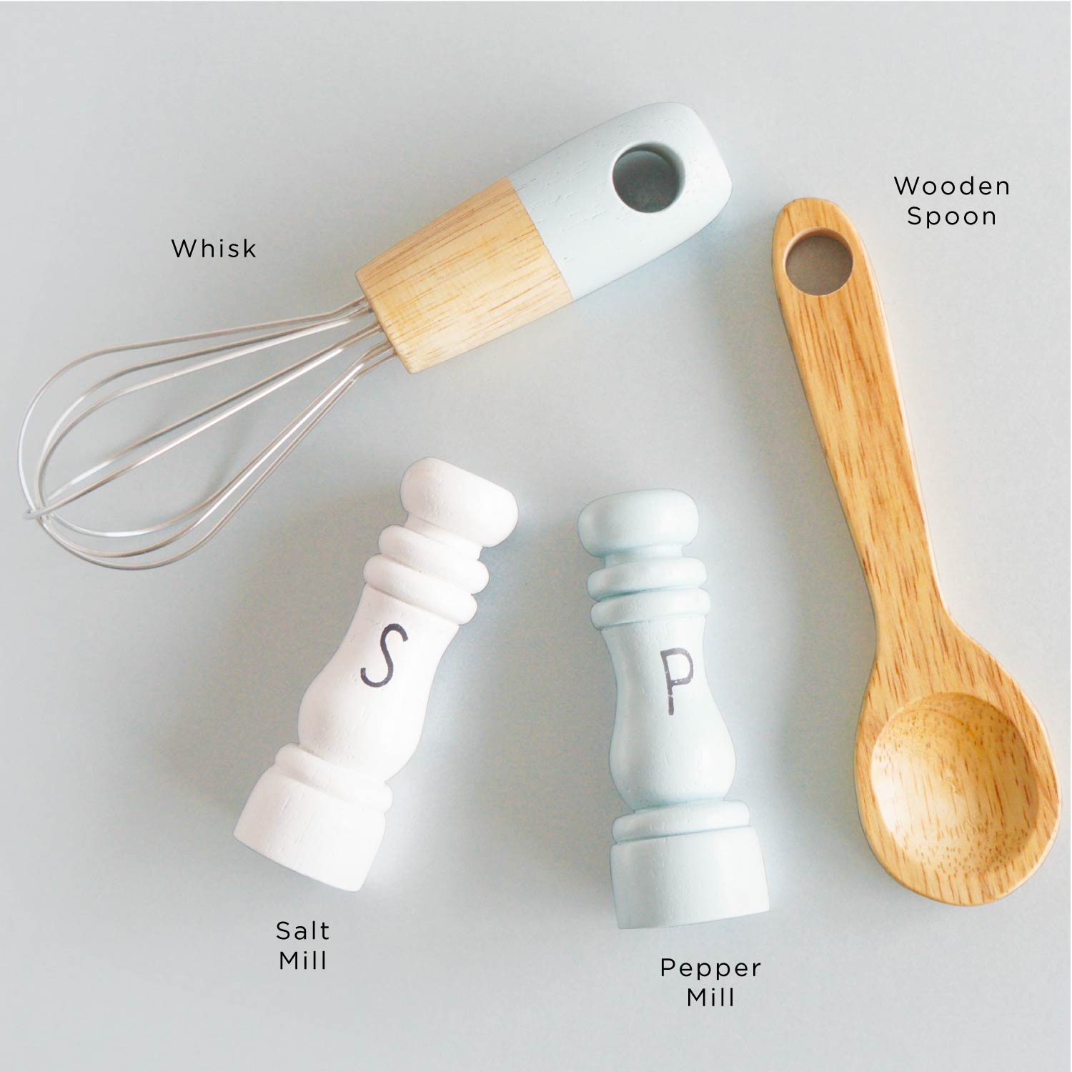 Set of kitchen utensils including a whisk, salt mill, pepper mill, and wooden spoon on a light gray background.