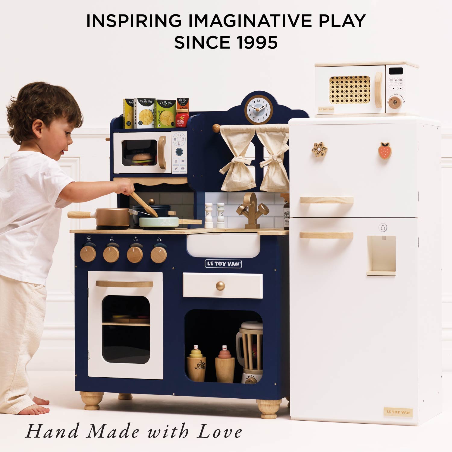 Child playing with a toy kitchen set, with text 'Inspiring Imaginative Play Since 1995' and 'Hand Made with Love'.