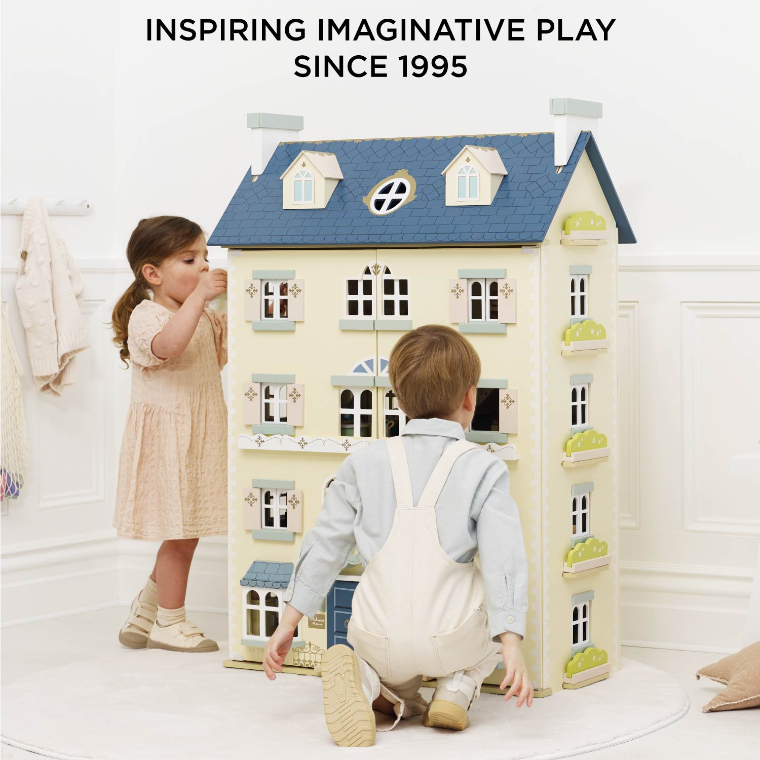 Children playing with a toy dollhouse in a bright room, with text 'Inspiring Imaginative Play Since 1995'.