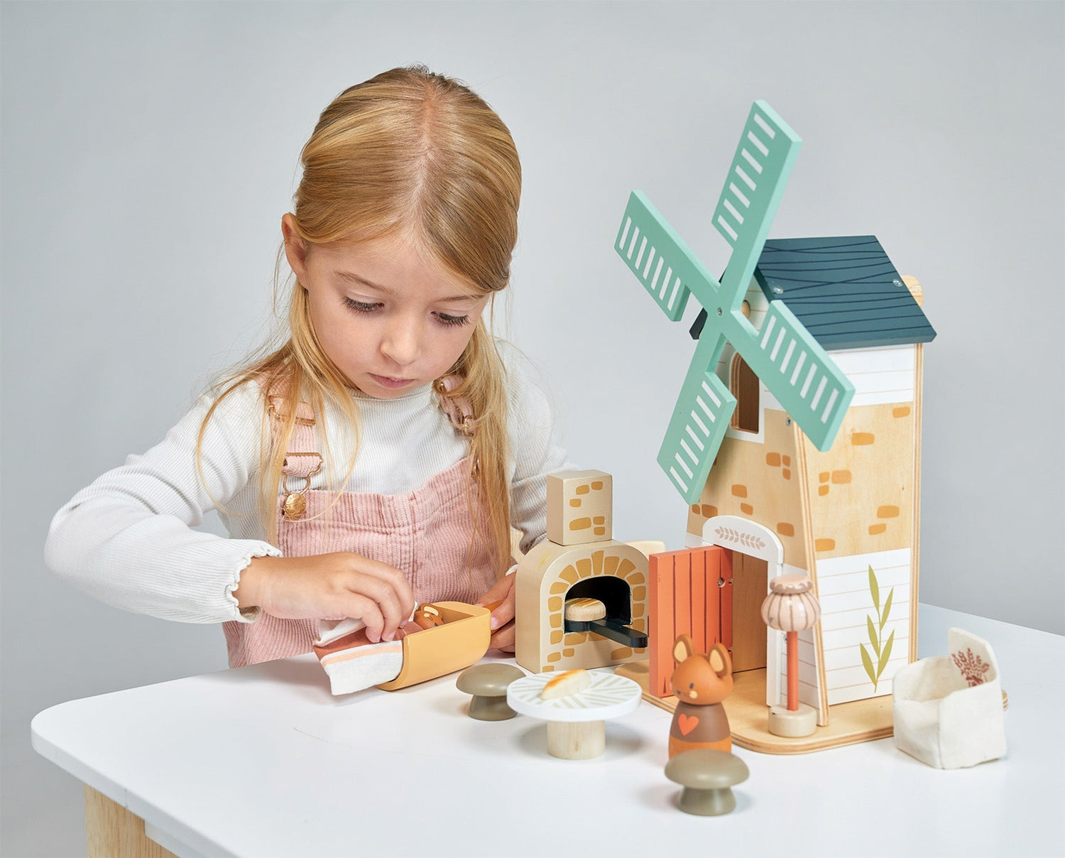 Young girl playing with a wooden toy set on a table, featuring a windmill and other structures.