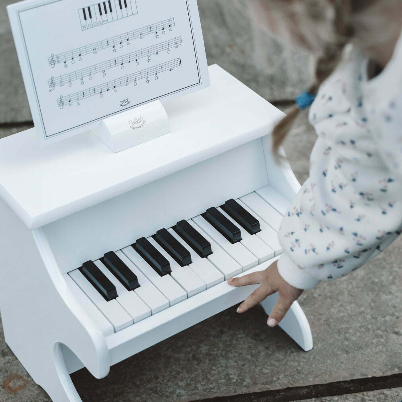 White toy piano with black keys and sheet music on a child's hand