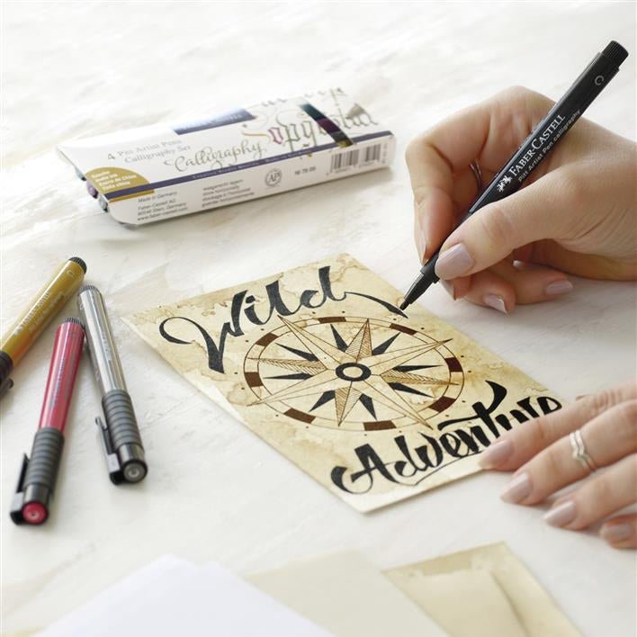 Hand holding a pen over a wooden engraving with calligraphy text on a white surface.