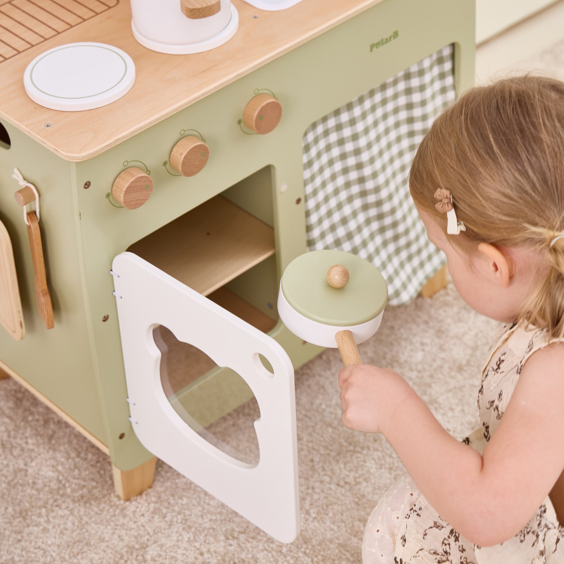 Child playing with a green toy kitchen set on a carpeted floor.