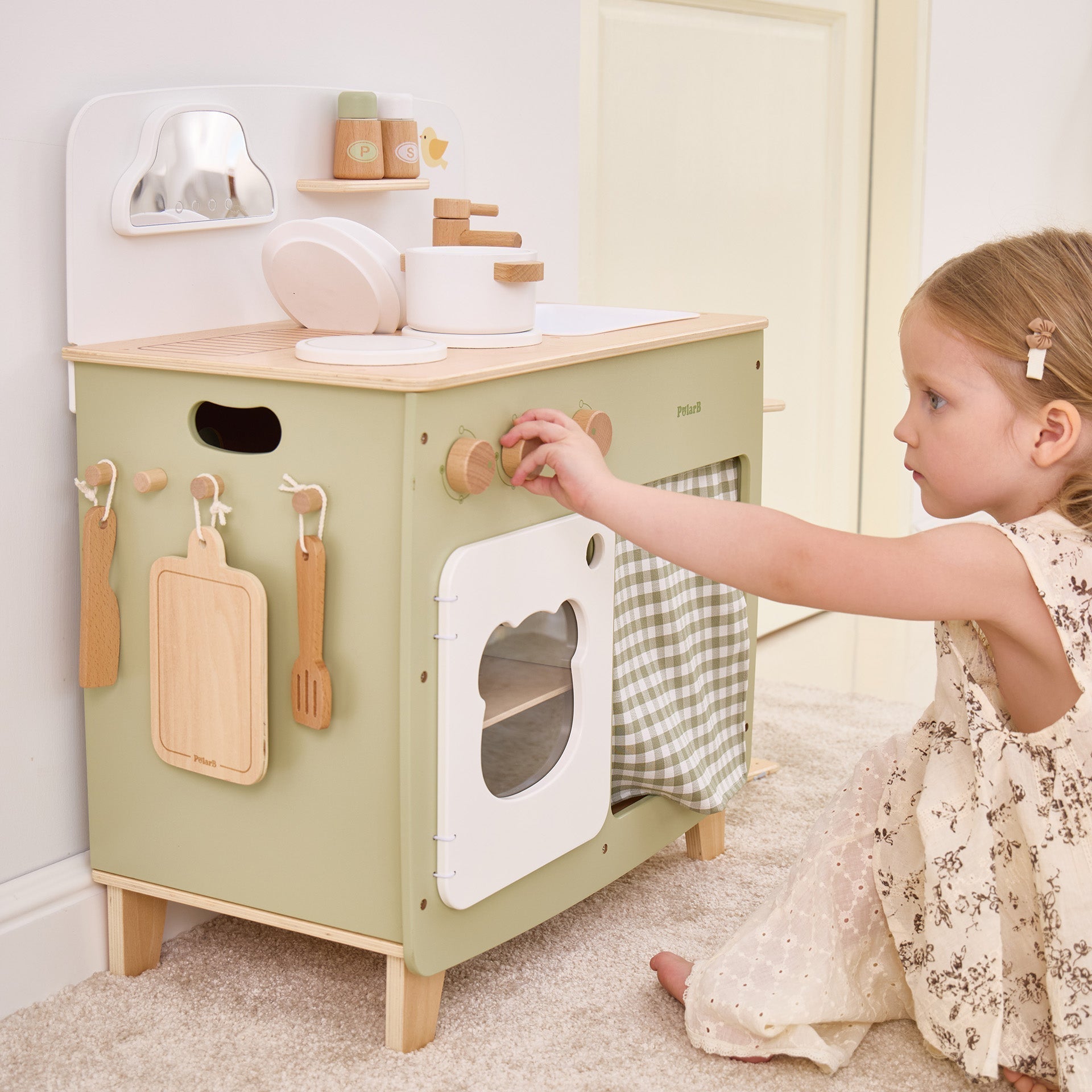 Child playing with a wooden toy kitchen set in a room.