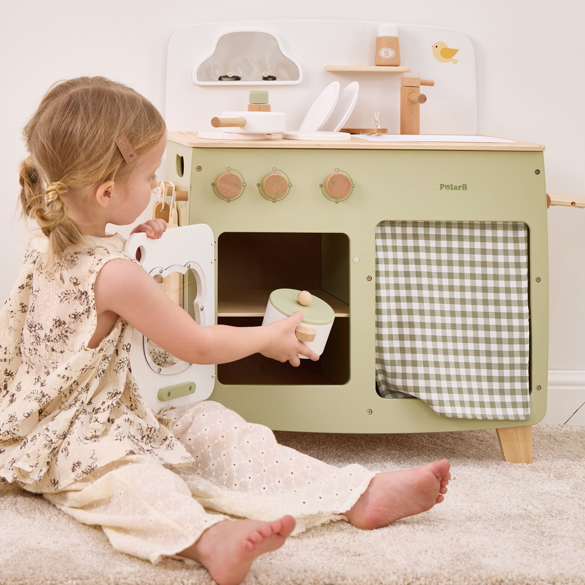 Child playing with a toy kitchen set on a carpeted floor.