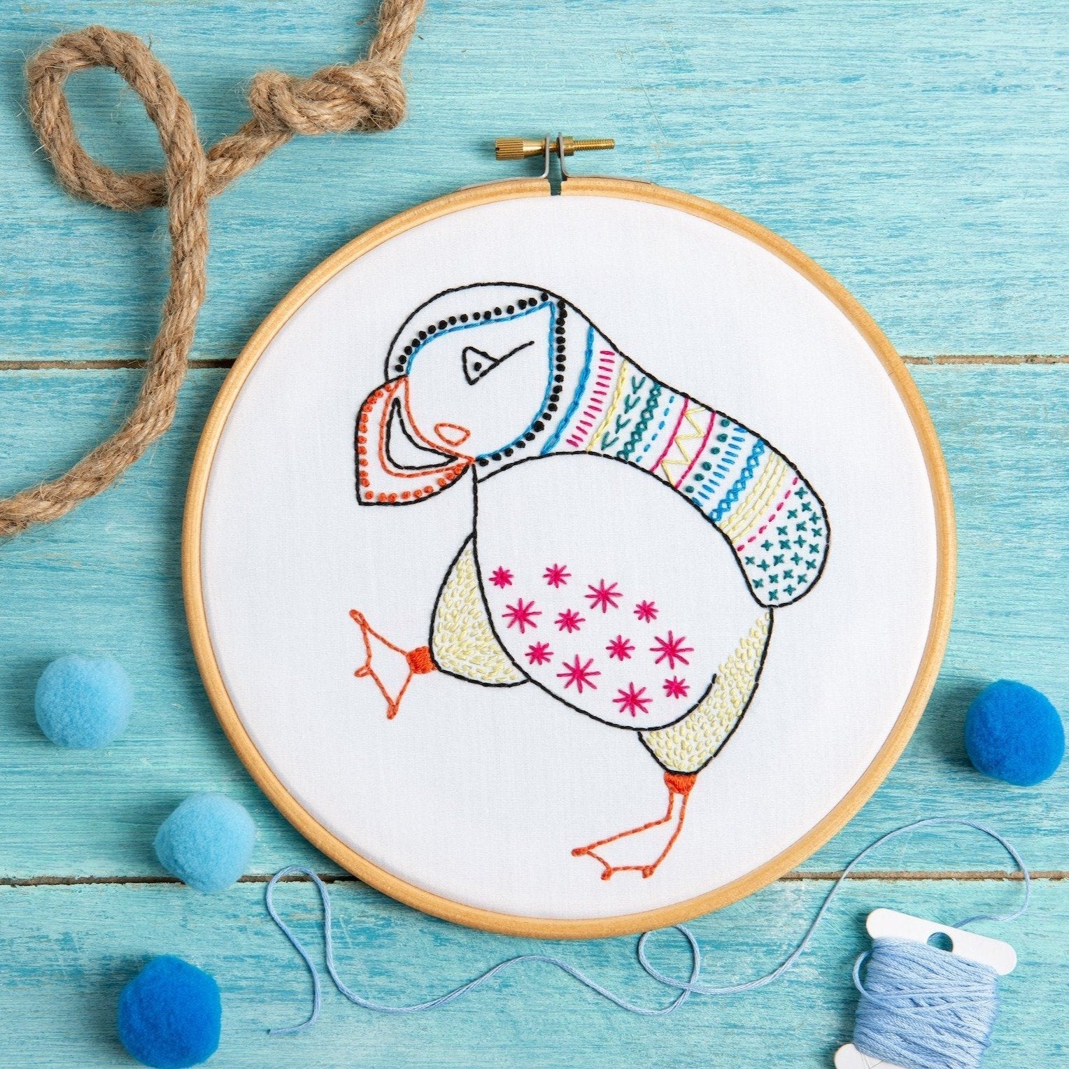 Embroidery hoop with a colorful bird design on a blue wooden surface