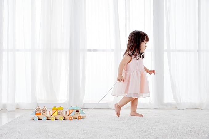 Child in a pink dress walking with a toy on a white floor and curtain background