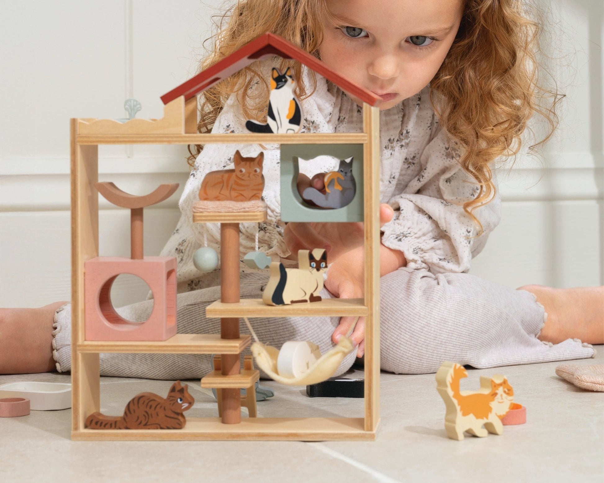 Child playing with a wooden toy house and animal figures on a light surface.