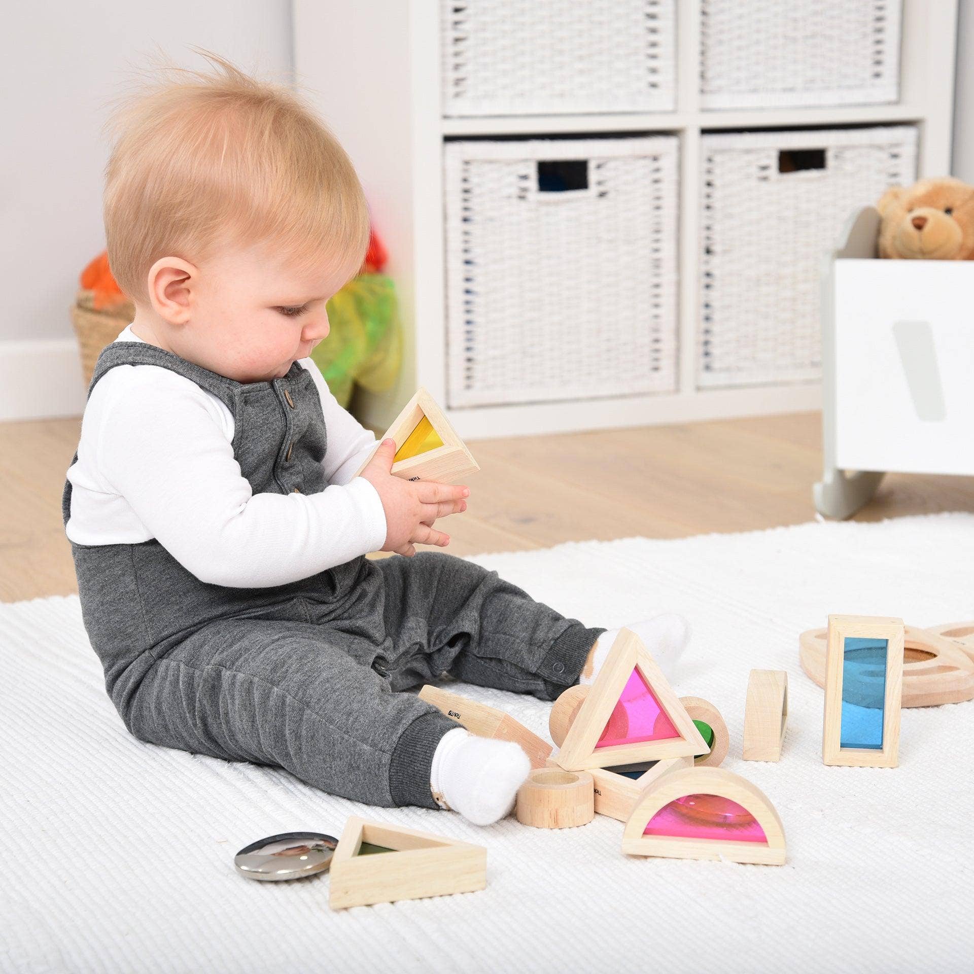 Child playing with wooden toys on a bed in a room with white storage units.