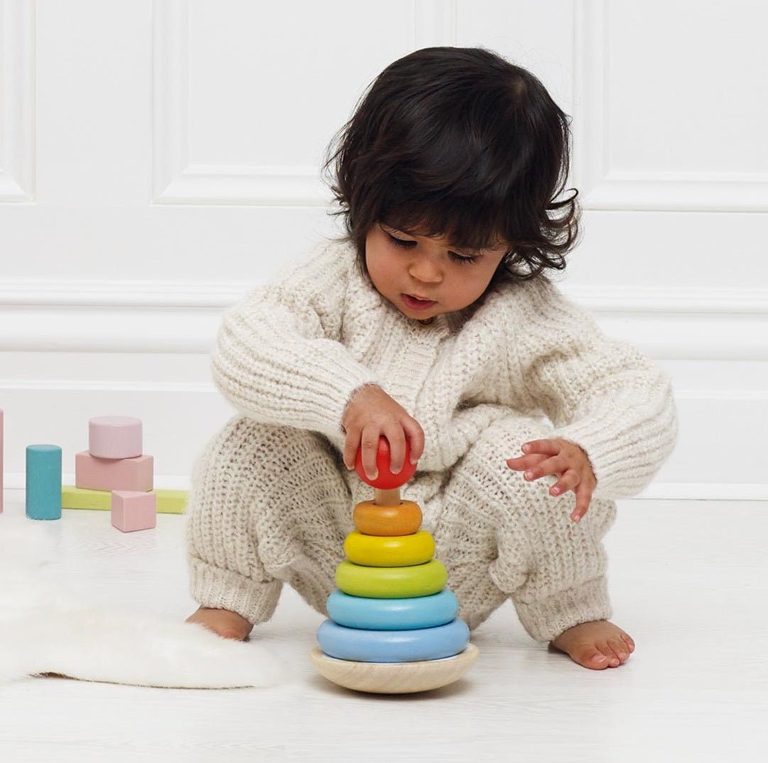Child playing with a colorful stacking toy on a white floor.