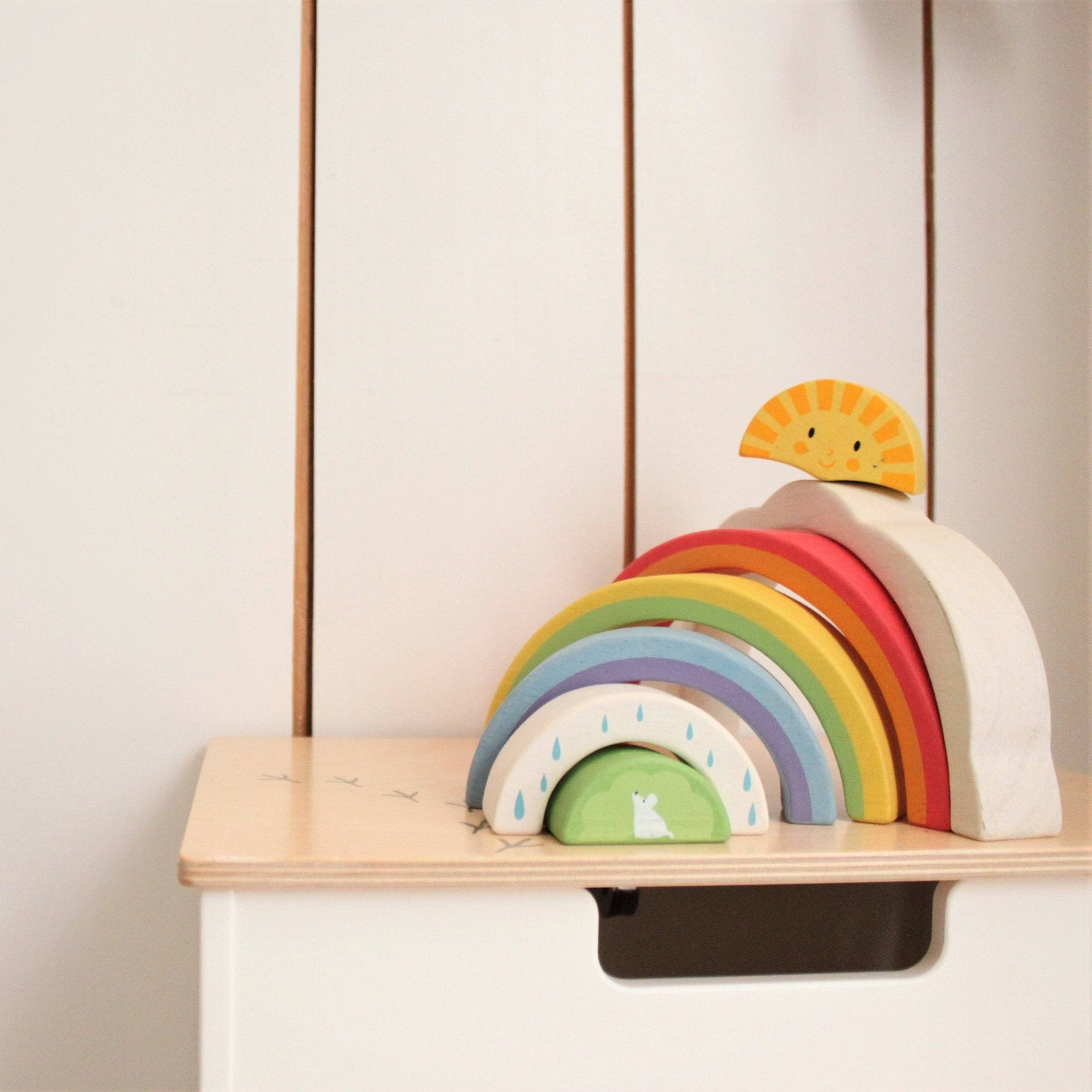 Wooden rainbow toy with a sun on a shelf against a neutral wall