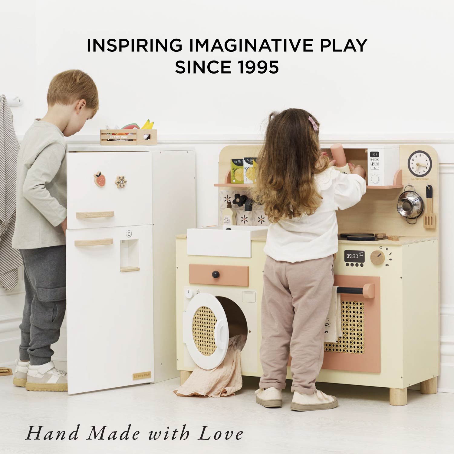 Children playing with a toy kitchen set, with text 'Inspiring Imaginative Play Since 1995' and 'Hand Made with Love'.