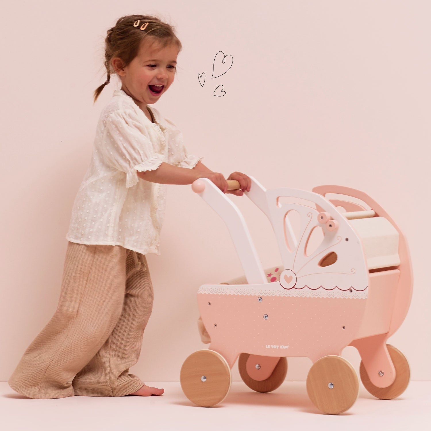 Child pushing a pink doll pram against a light pink background