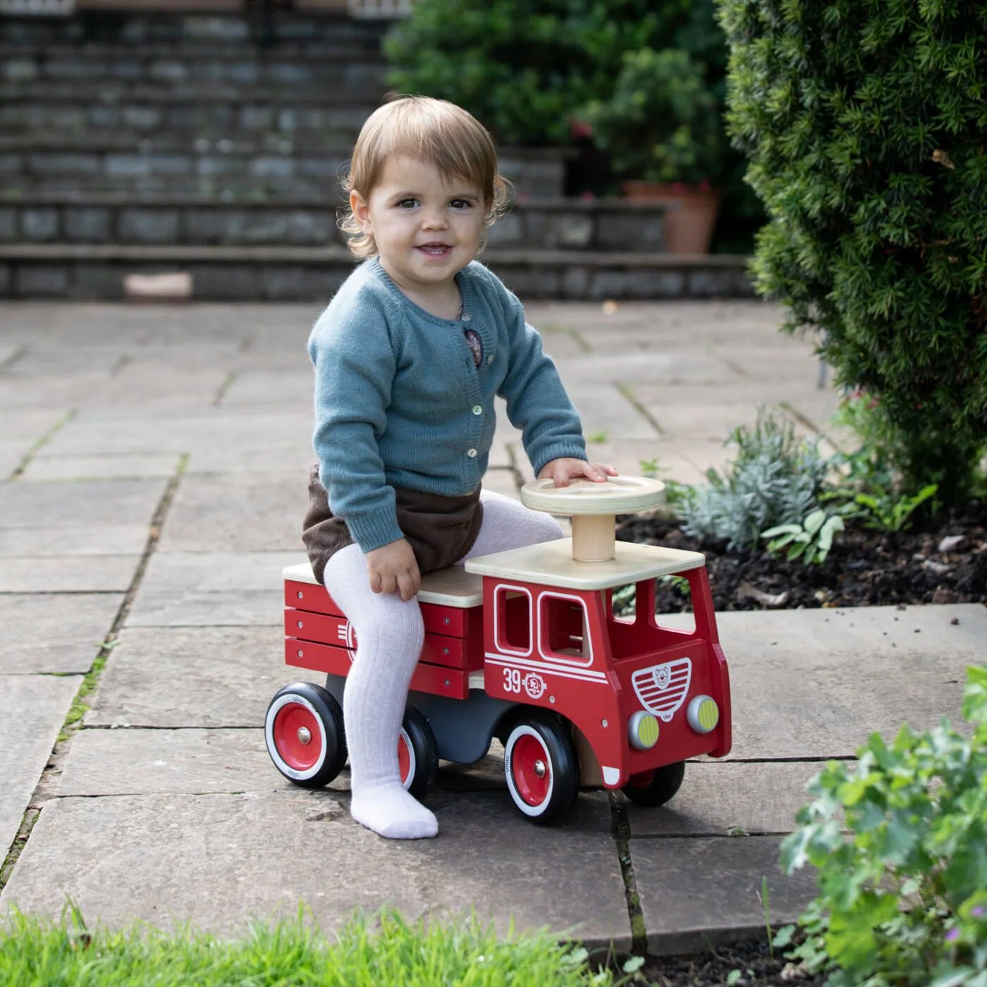 Child sitting on a red toy fire truck outdoors