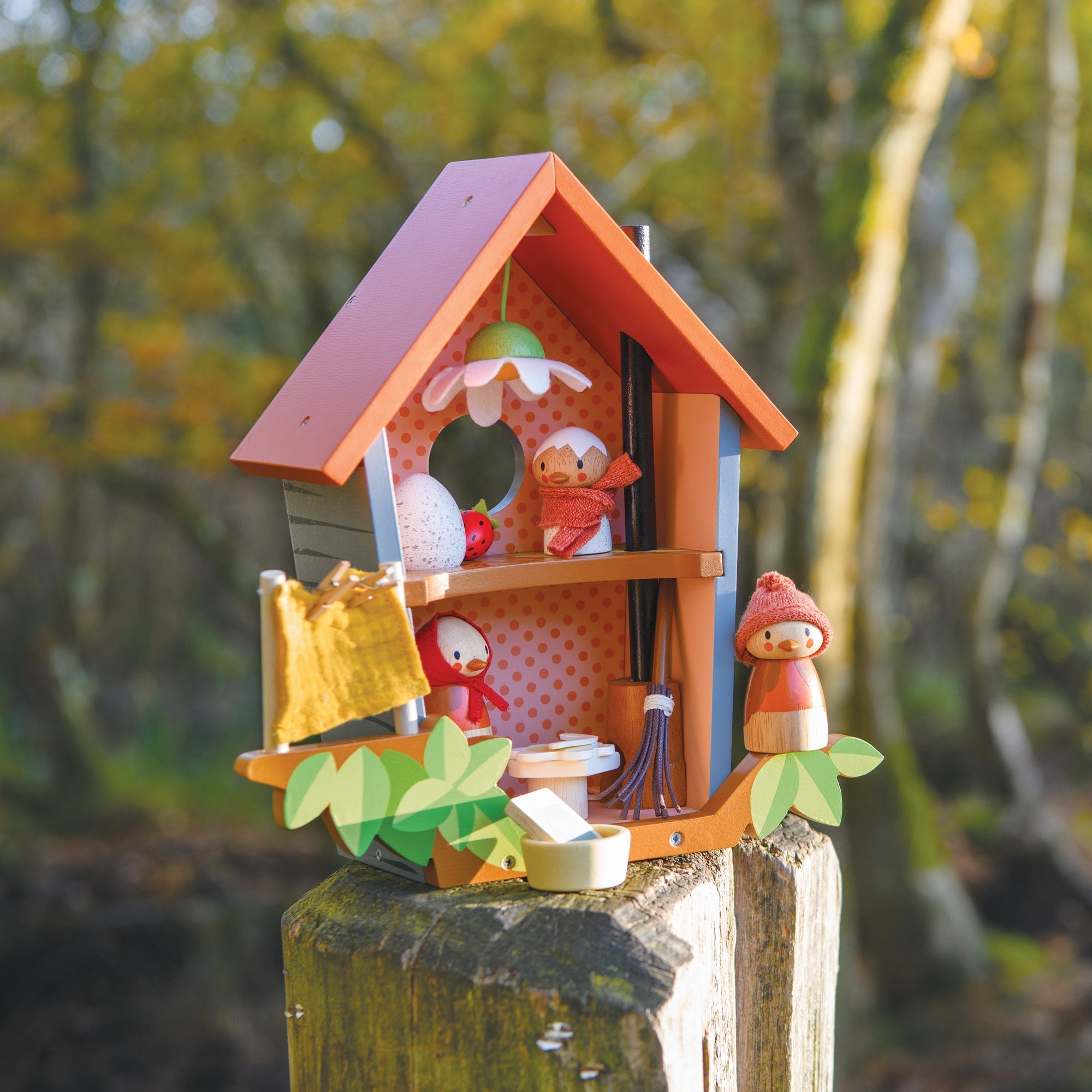 Colorful birdhouse with small figurines on a wooden post against a natural background
