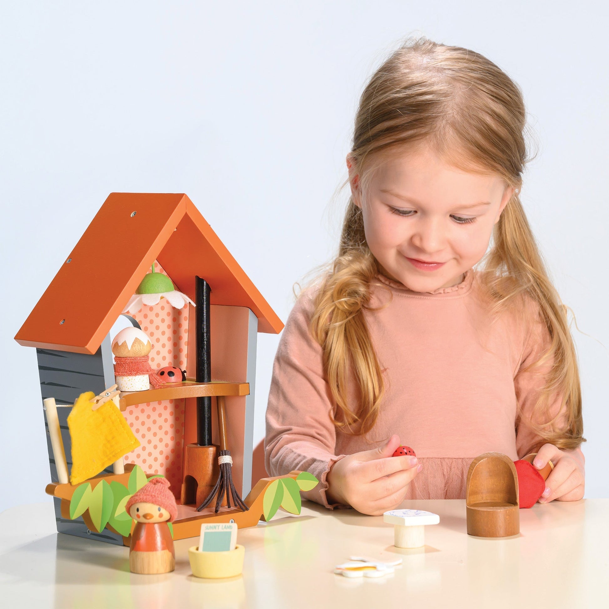 Young girl playing with a wooden dollhouse and accessories on a light blue background