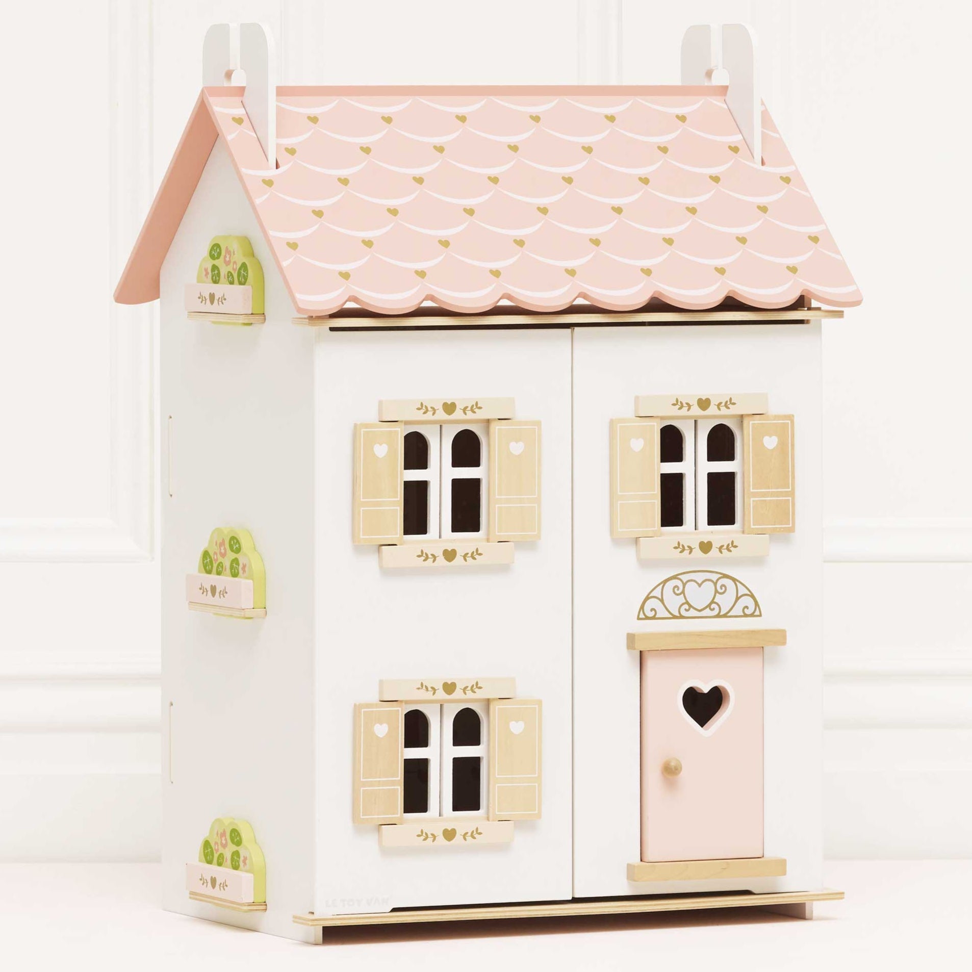 Small wooden dollhouse with a pink roof and white walls on a white background
