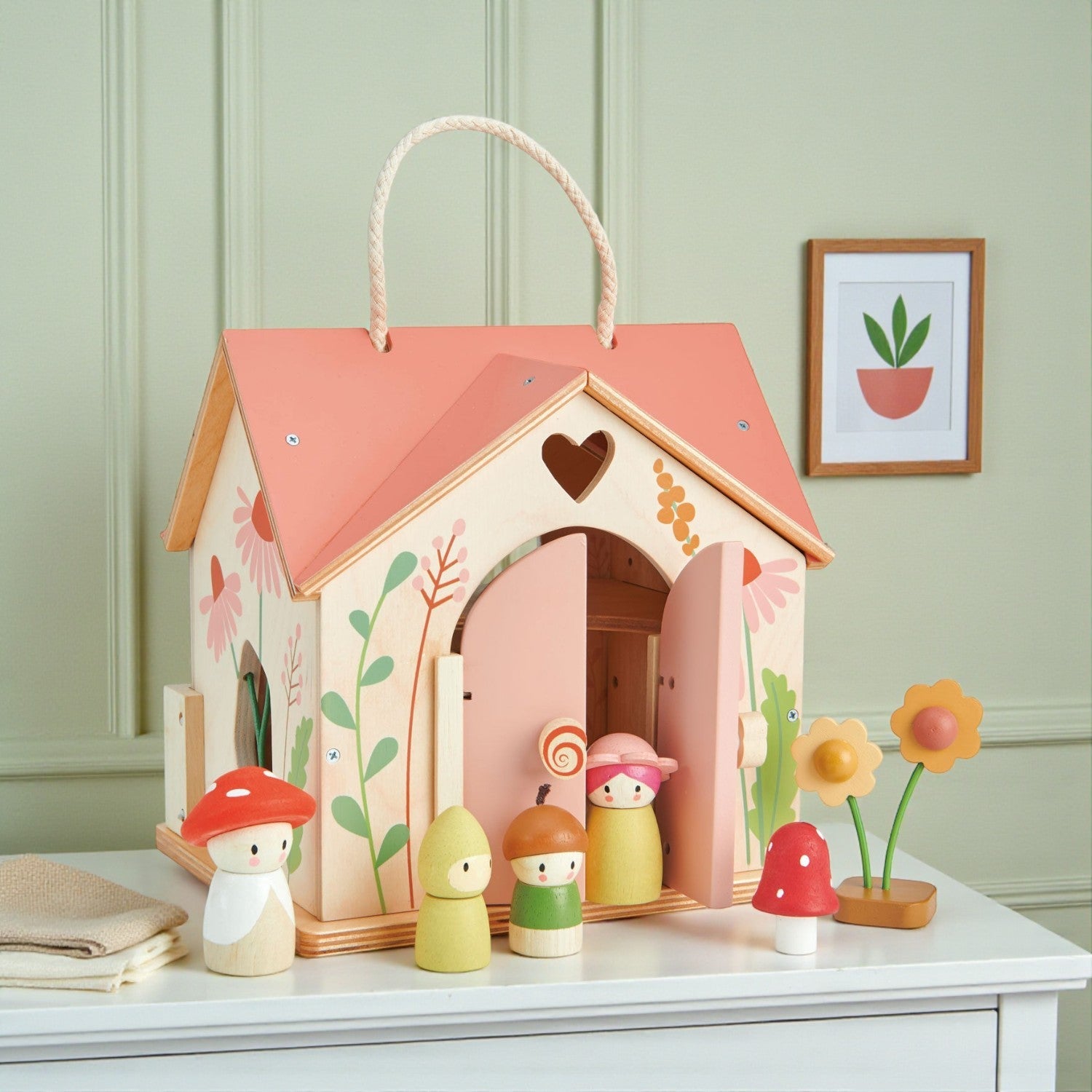 Wooden toy house with colorful characters and plants on a white surface.