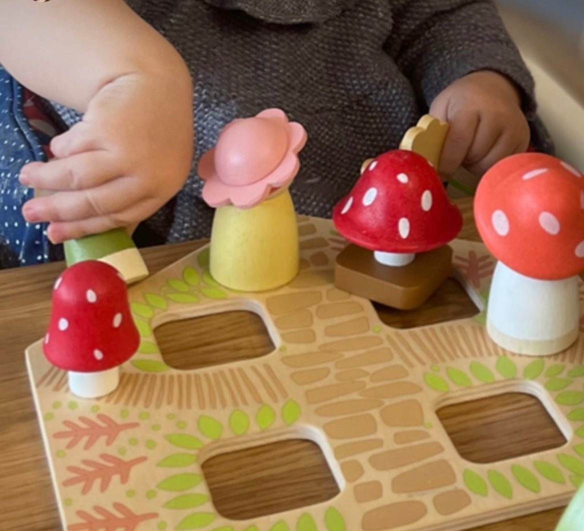 Children playing with a wooden mushroom puzzle on a wooden surface.