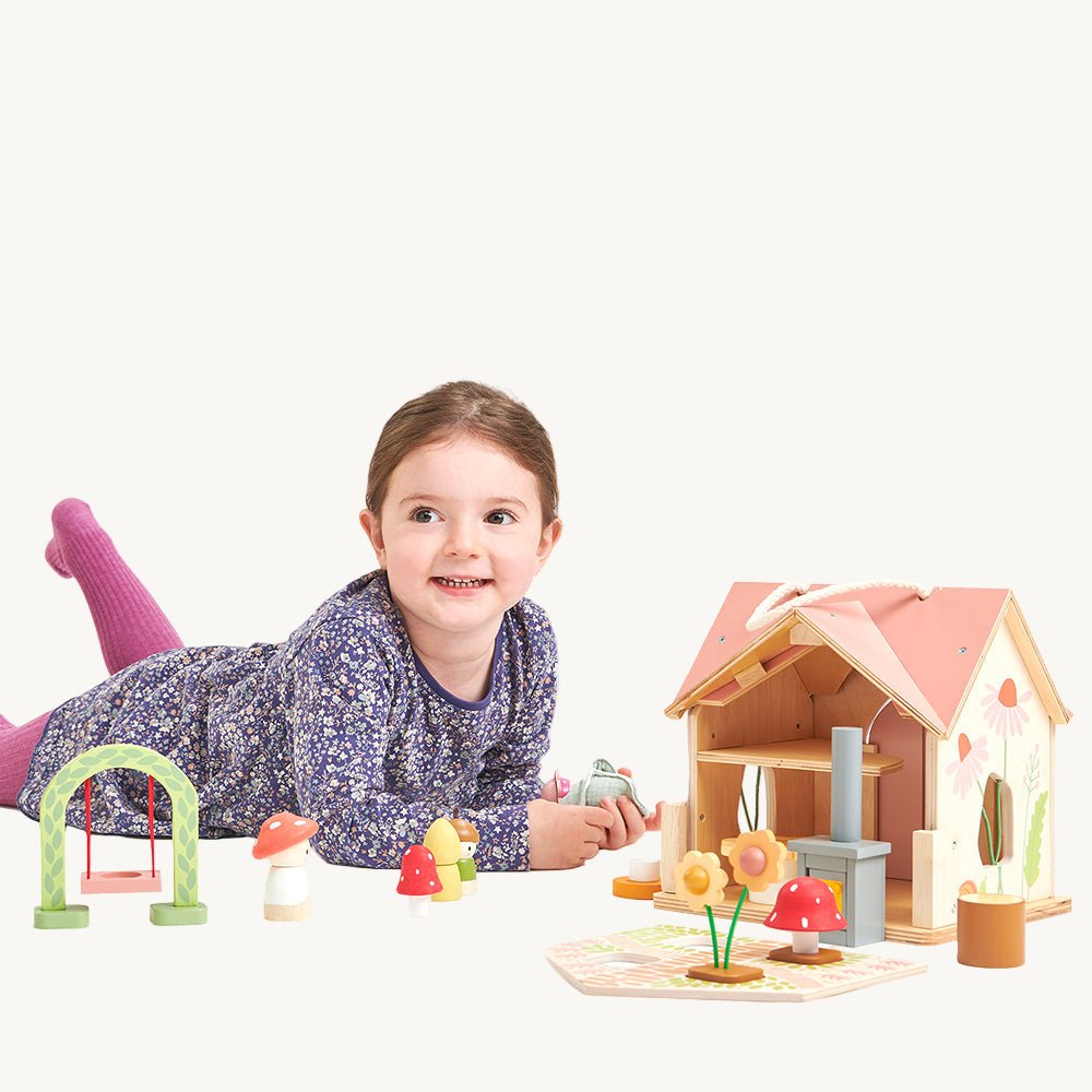 Child playing with a wooden dollhouse and accessories on a white background