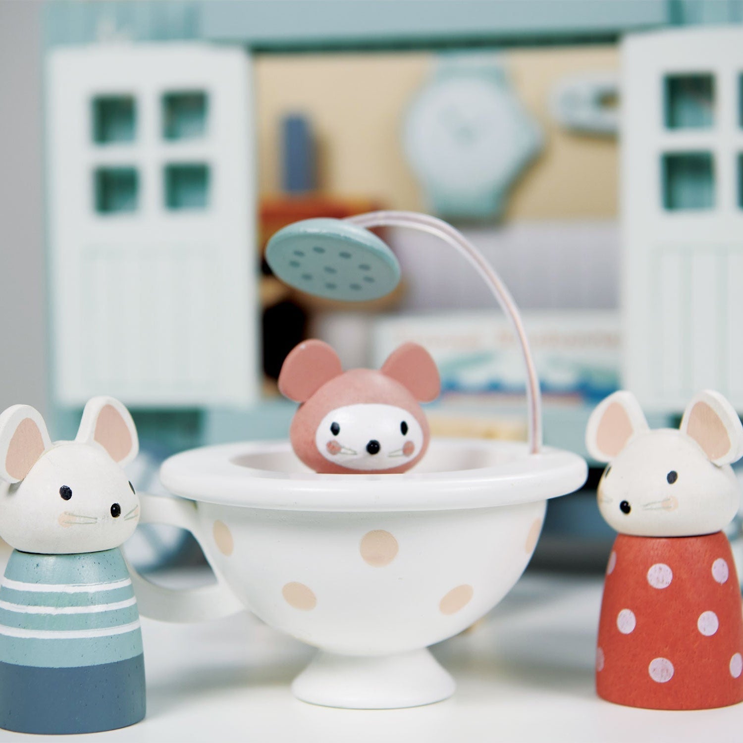 Wooden toy figures of mice in a bathtub with a shower head, set against a blurred background.