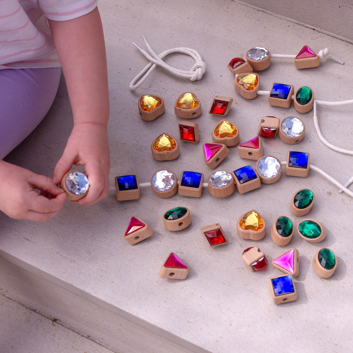 Child playing with colorful wooden gemstones on a light surface