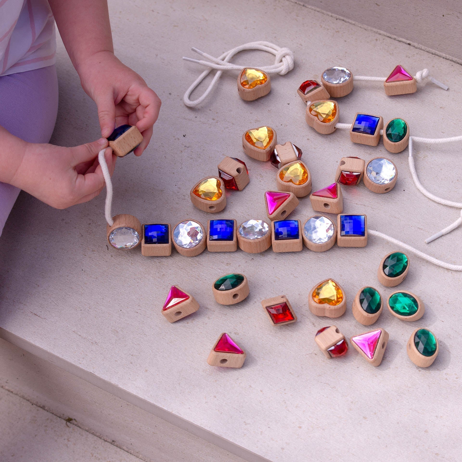 Colorful gemstone beads on a string with a child's hands interacting with them.