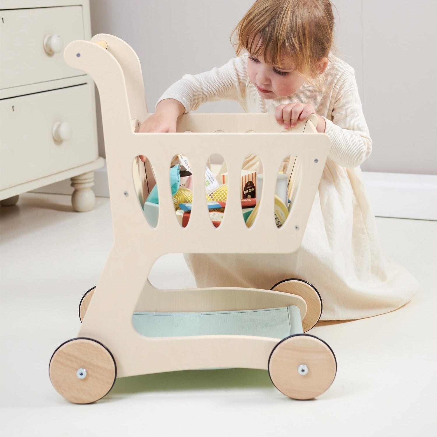 Child playing with a wooden toy cart in a room with white furniture.