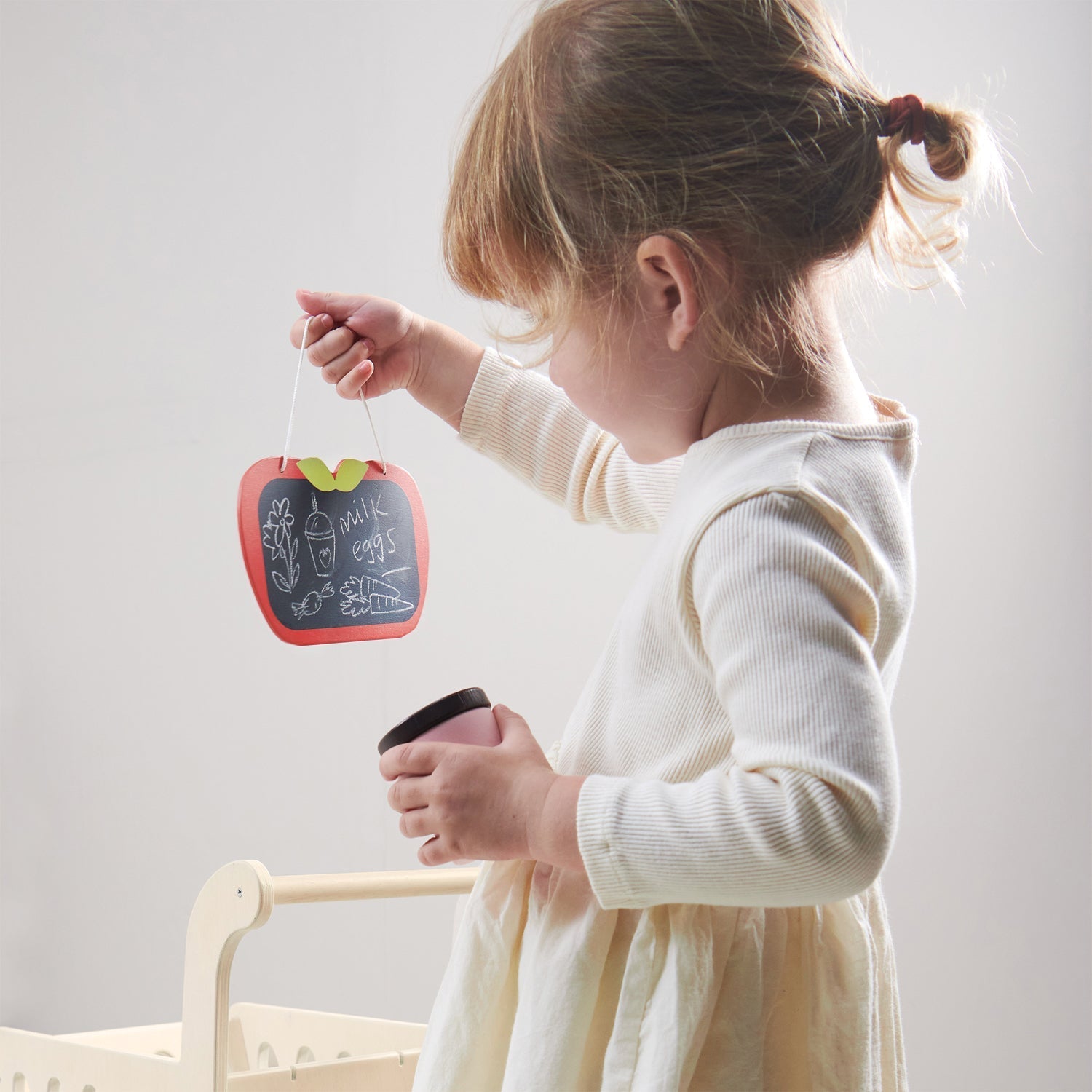 Child holding a small chalkboard with a red frame and green leaves, against a plain background.
