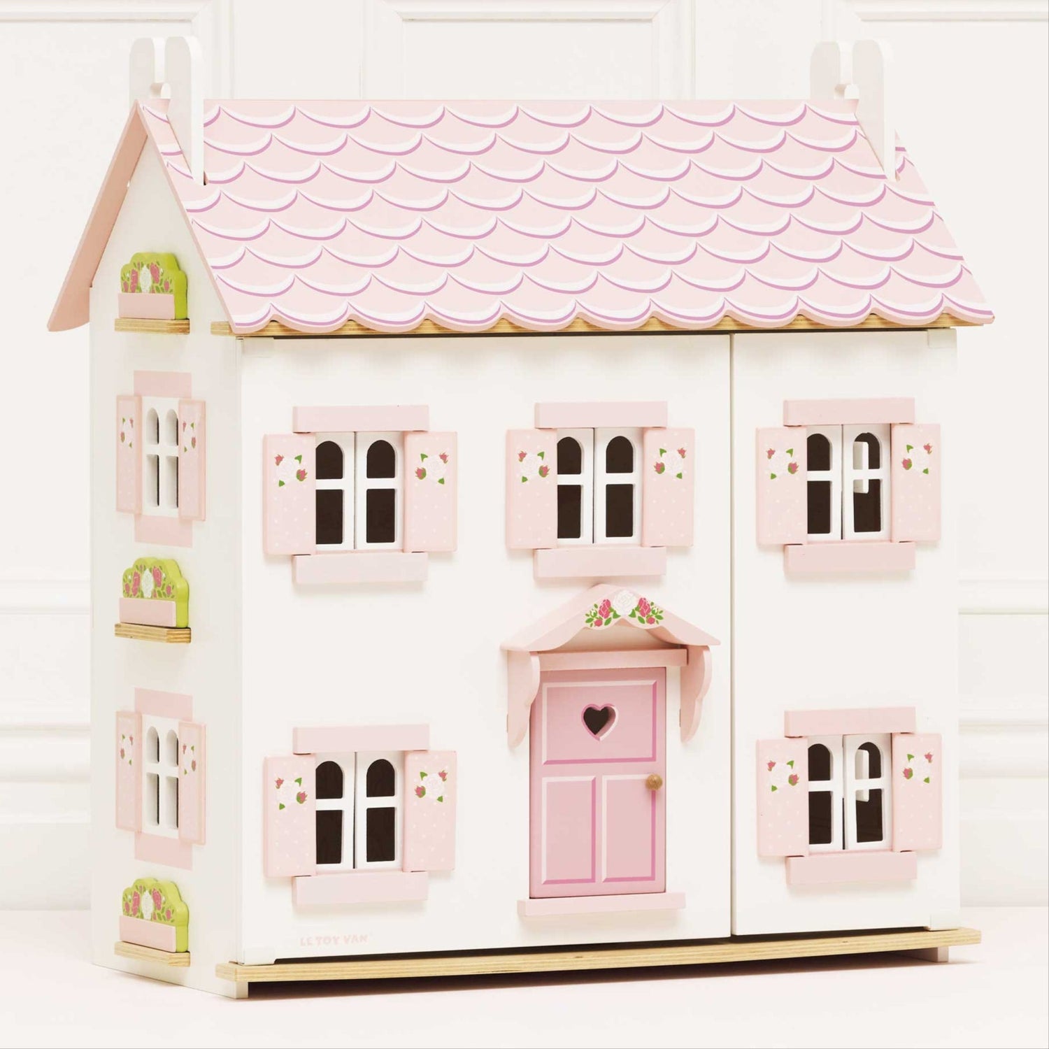Pink and white dollhouse with a scalloped roof on a white background