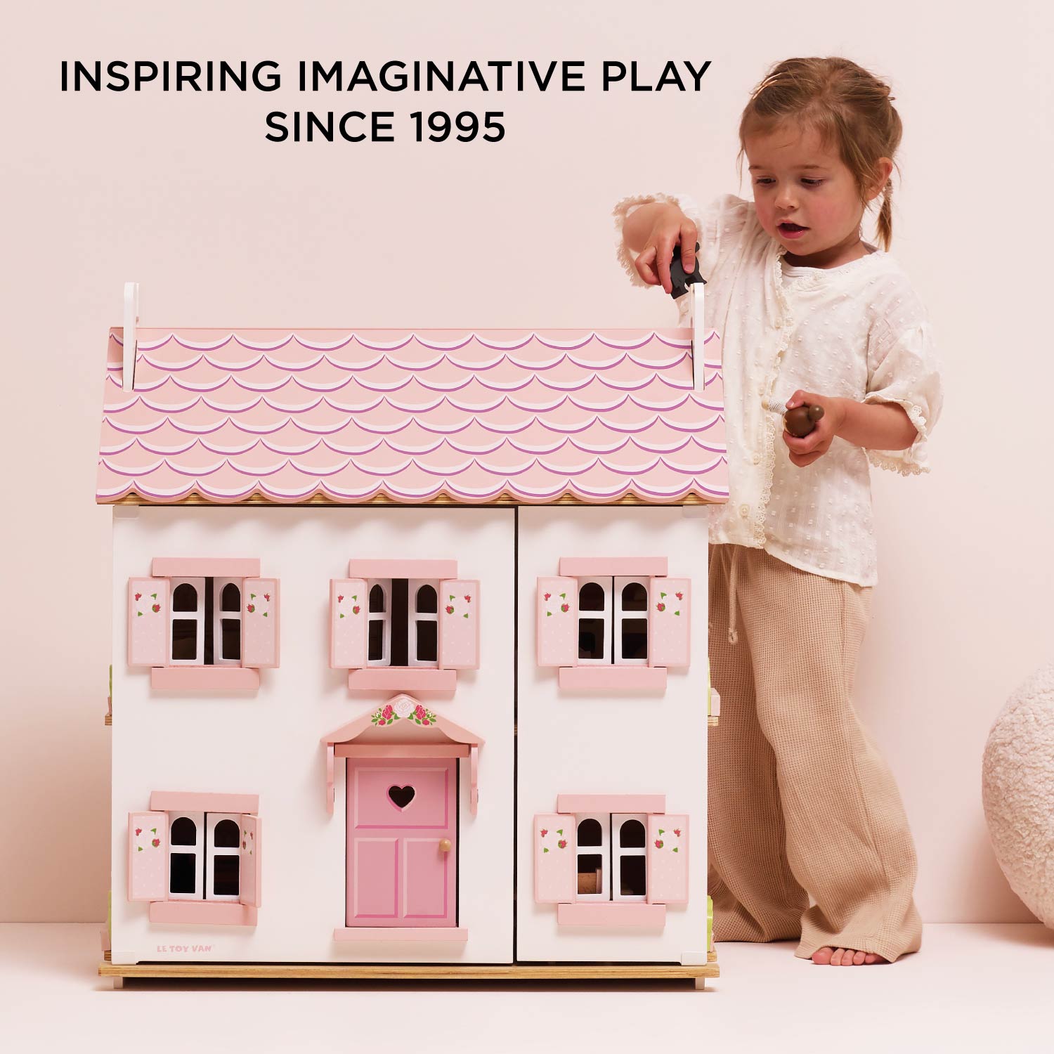 Child playing with a pink dollhouse, inspired by imaginative play since 1995.
