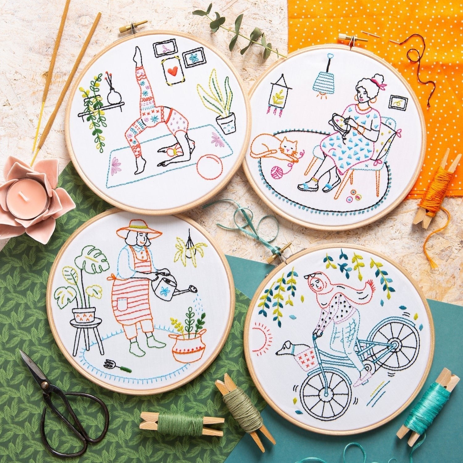 Four embroidery hoops with colorful designs on a textured surface with sewing tools.