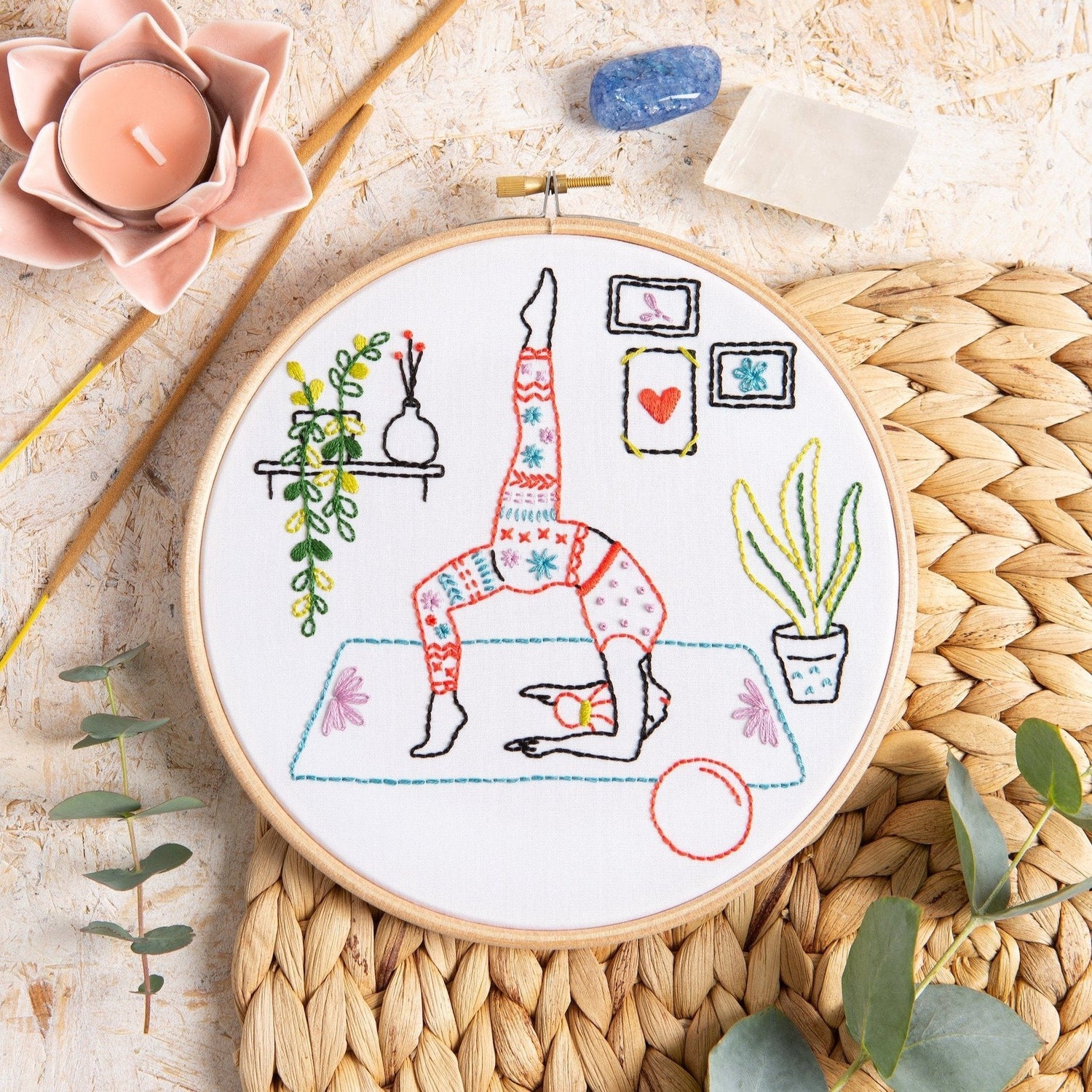 Embroidery hoop with a colorful illustration of a person doing yoga on a textured surface.