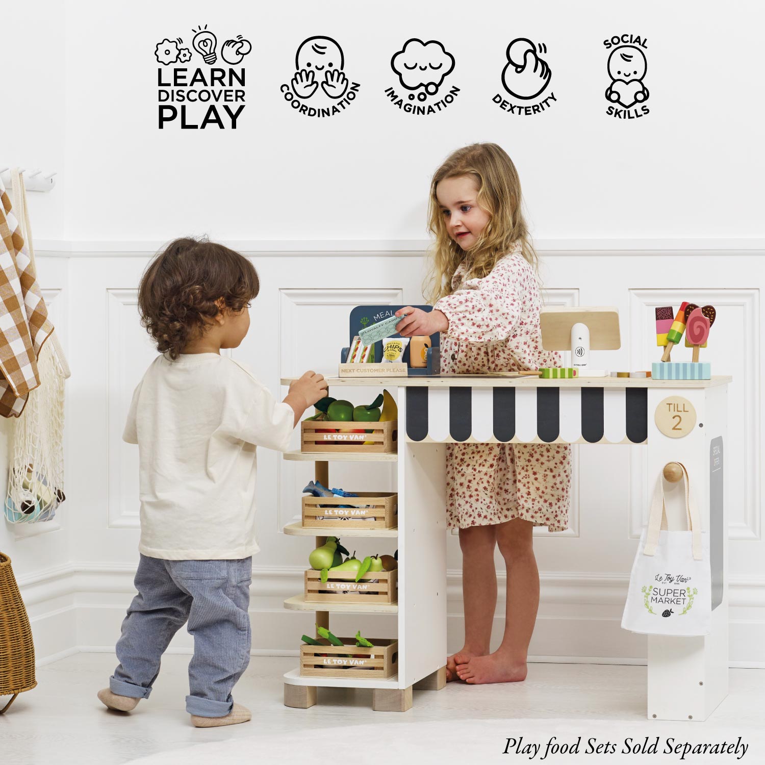Two children playing with a toy kitchen set in a room with educational icons above.