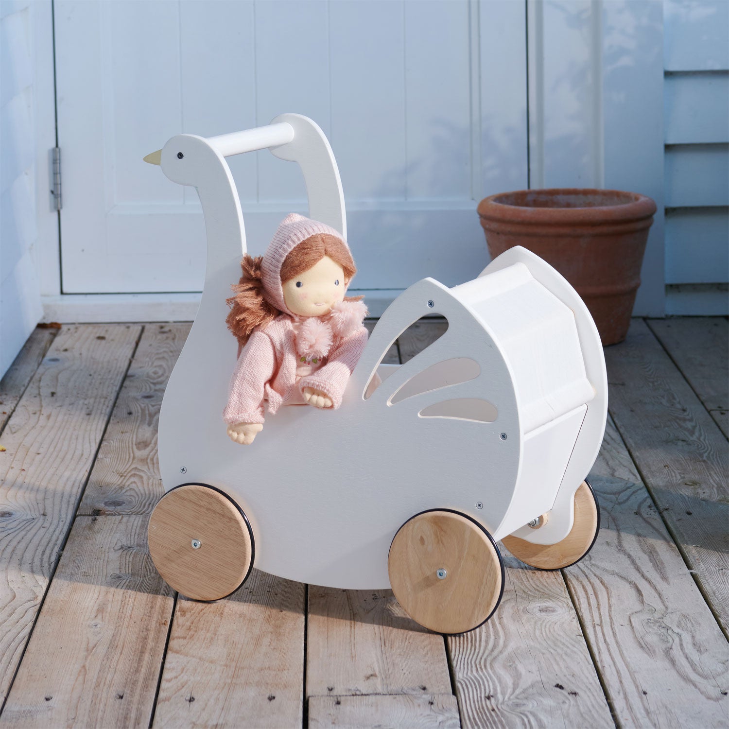 White wooden doll pram with a doll inside on a wooden floor.