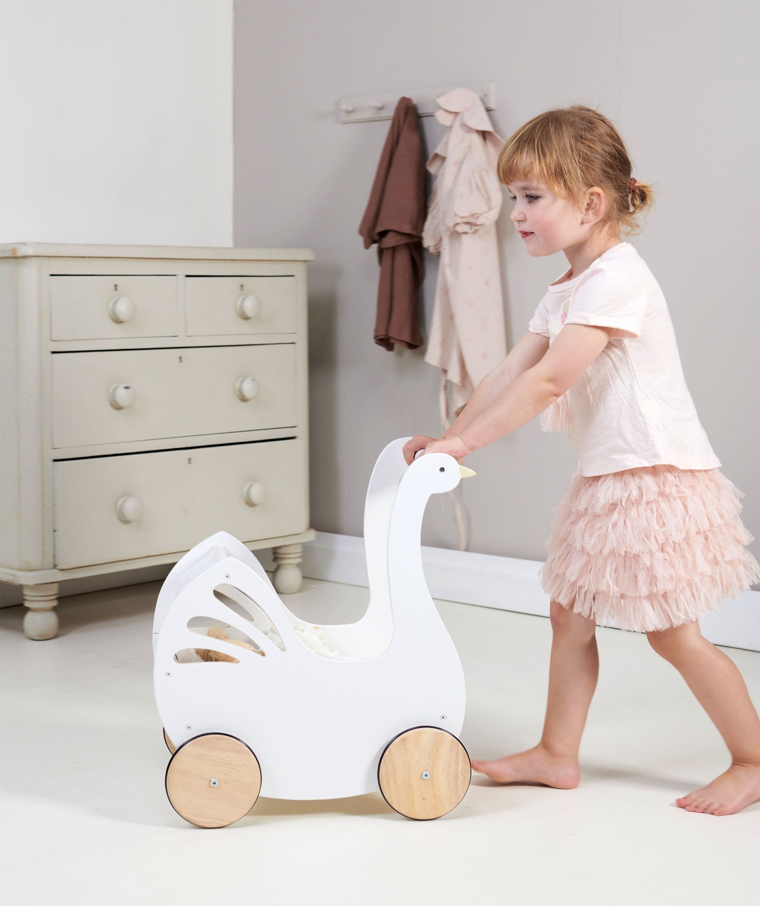 Child playing with a white goose-shaped toy in a room with a dresser and coat rack.