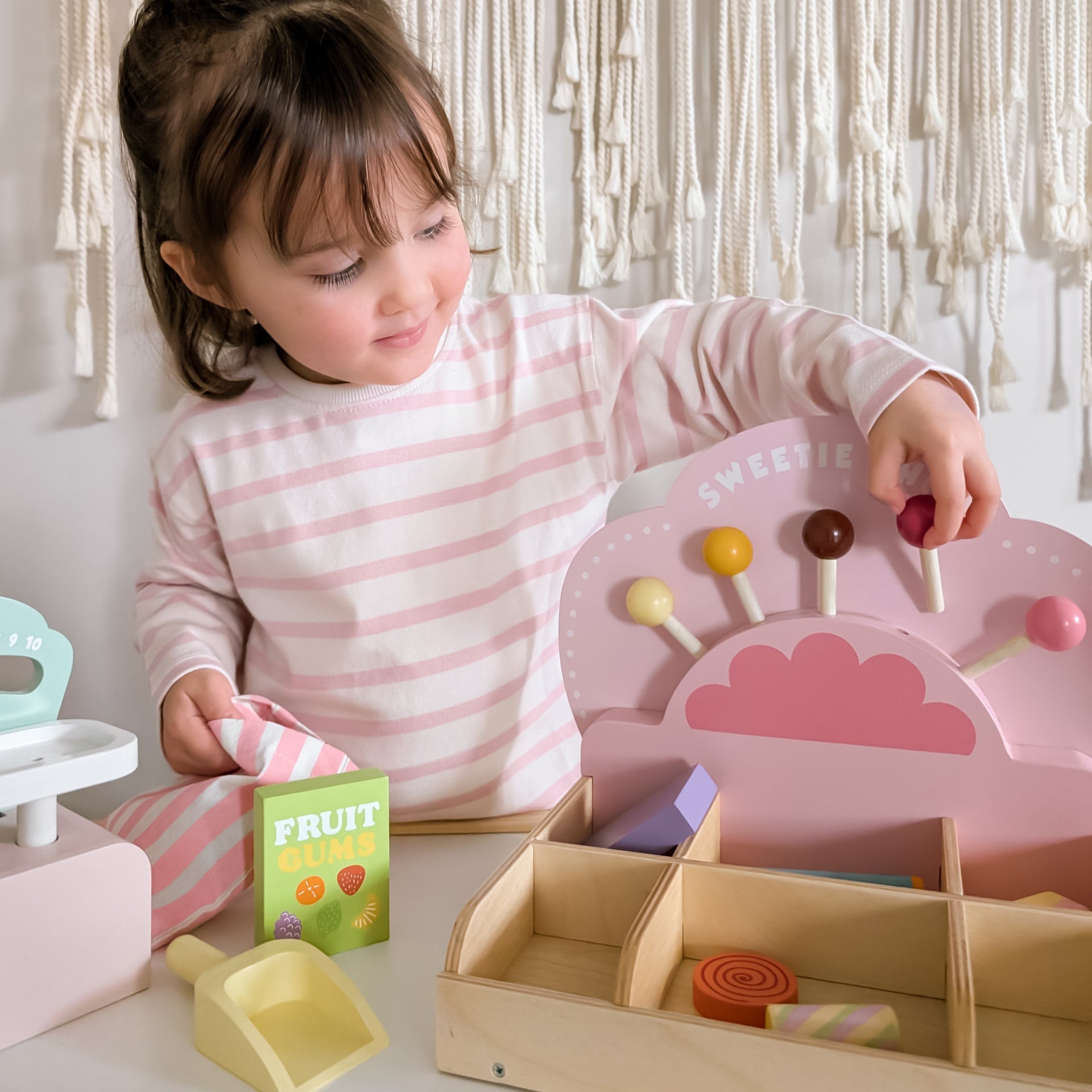 Child playing with a wooden toy set, including a pink sorting tray and colorful candies.