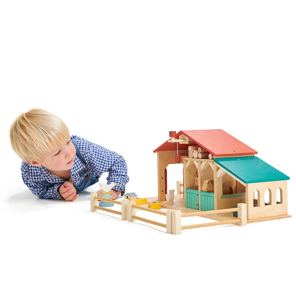 Child playing with a colorful wooden toy barn on a white background