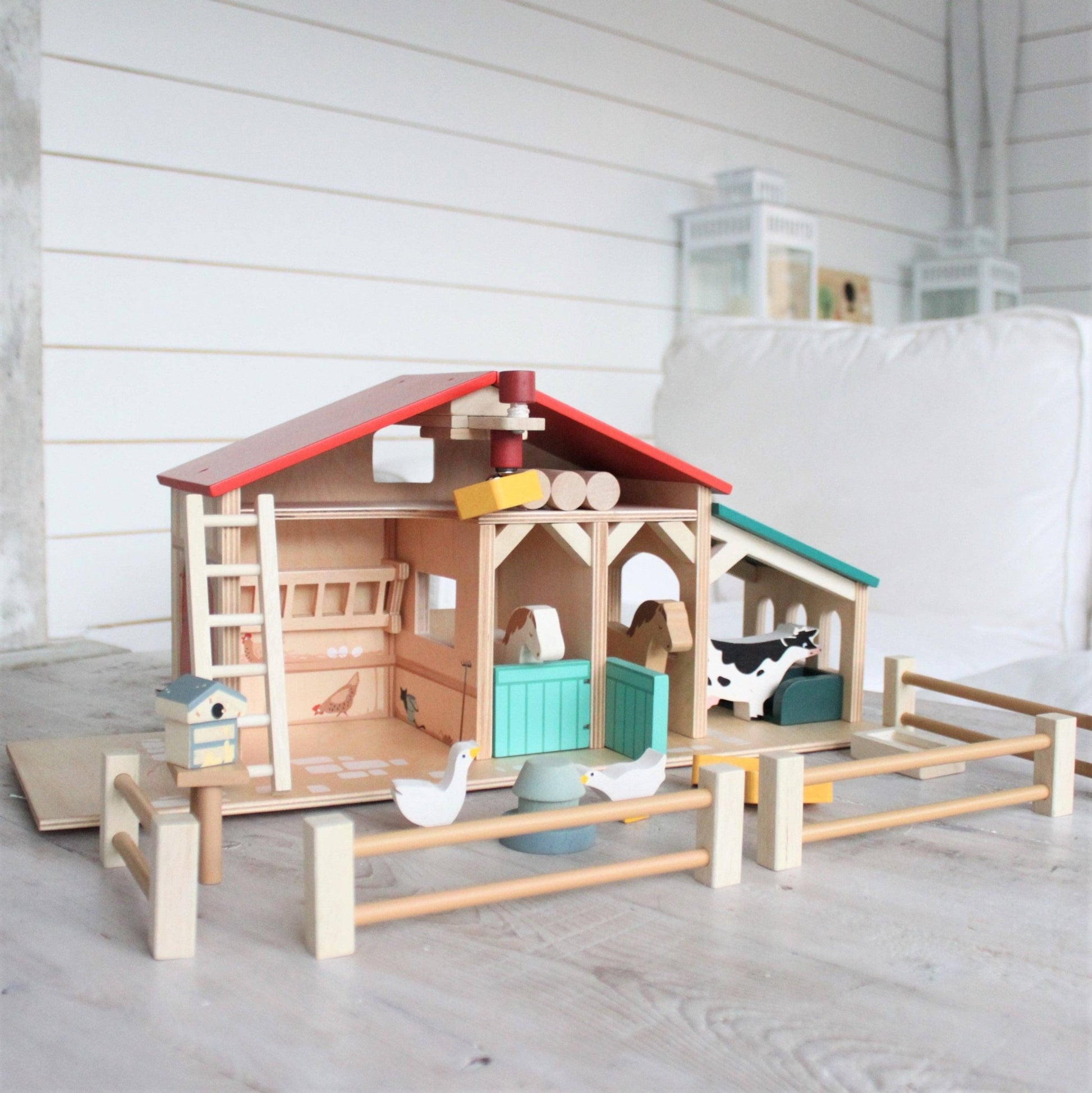 Wooden toy barn with animals on a light wooden floor.