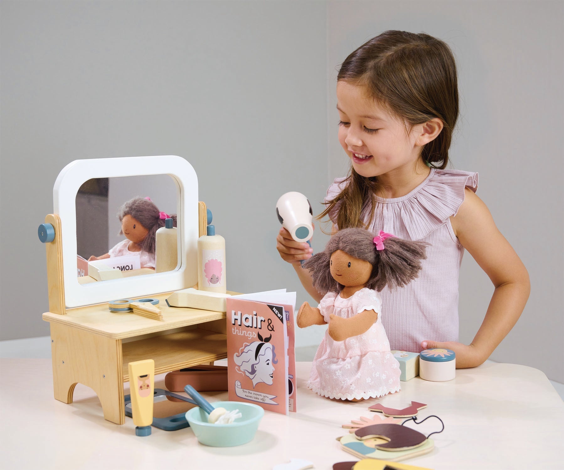 Child playing with a doll and toy vanity set on a table.