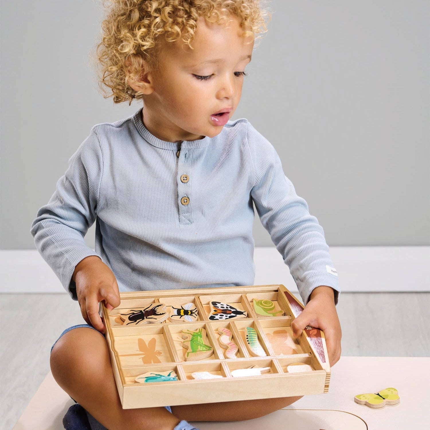 Child playing with a wooden puzzle toy on a light-colored surface.