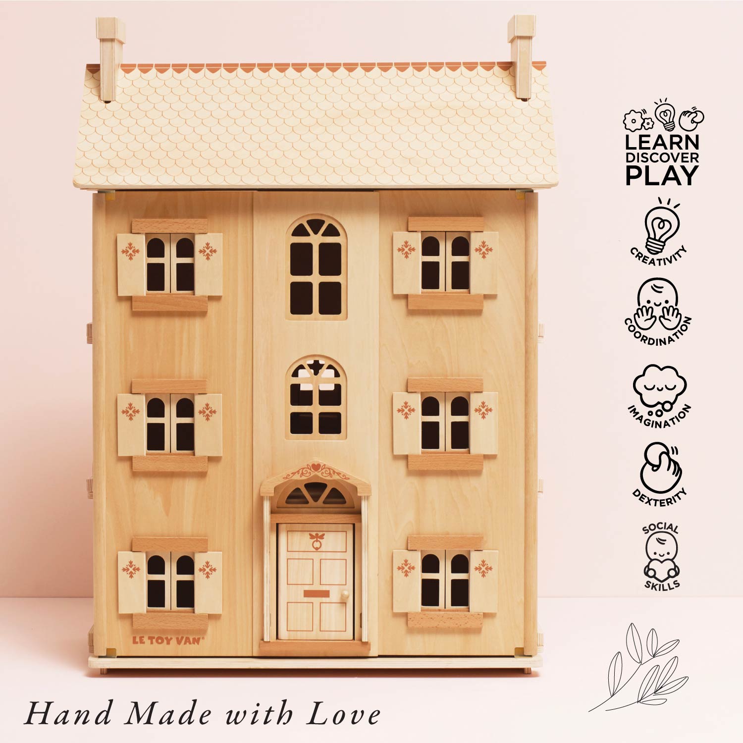 Wooden dollhouse with 'Le Toy Van' branding on a light pink background, featuring educational icons and 'Hand Made with Love' text.