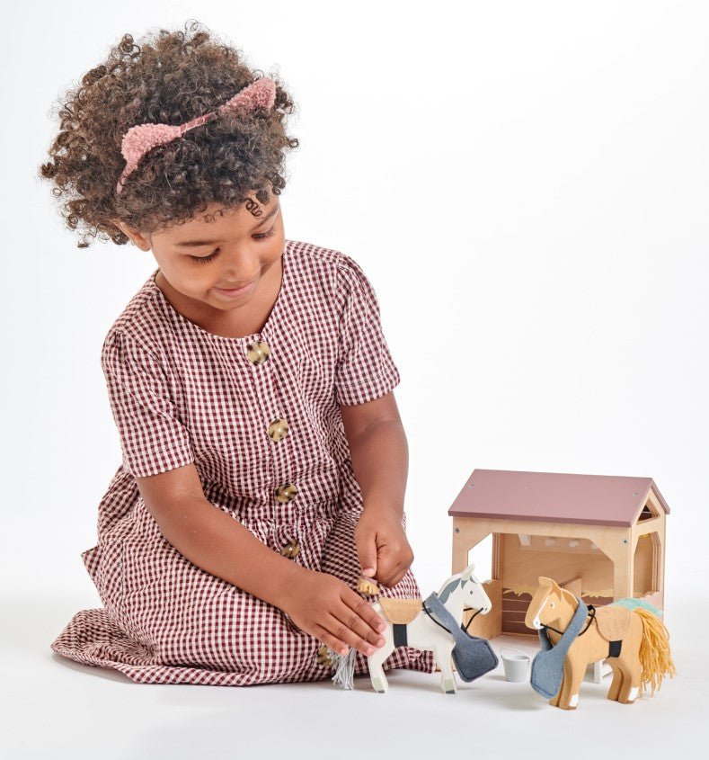 Child playing with toy horses and a small house on a white background