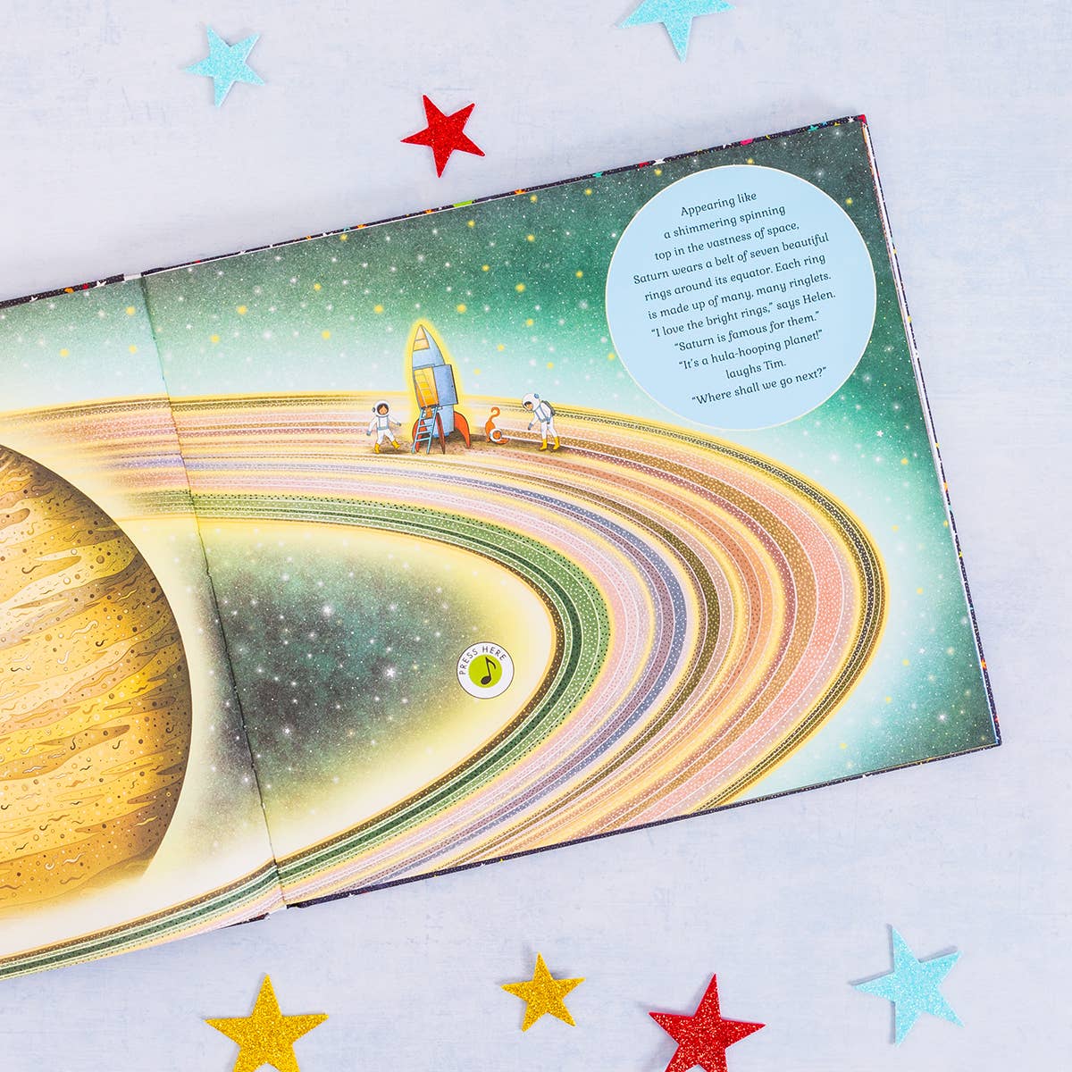 Children's book open to a page with a space-themed illustration, including a planet and astronauts.