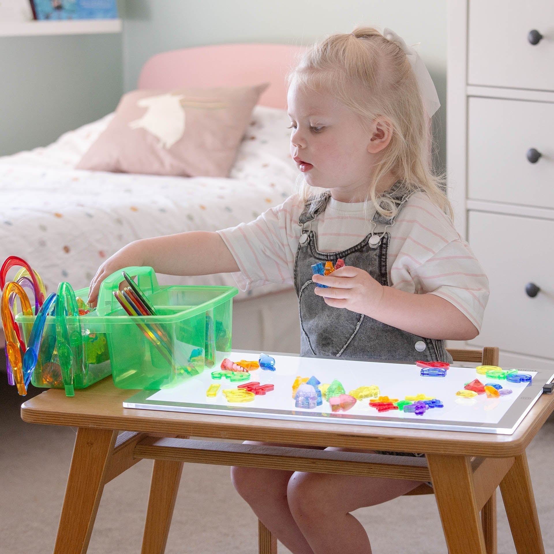 Child playing with colorful magnetic letters on a table in a bedroom setting.