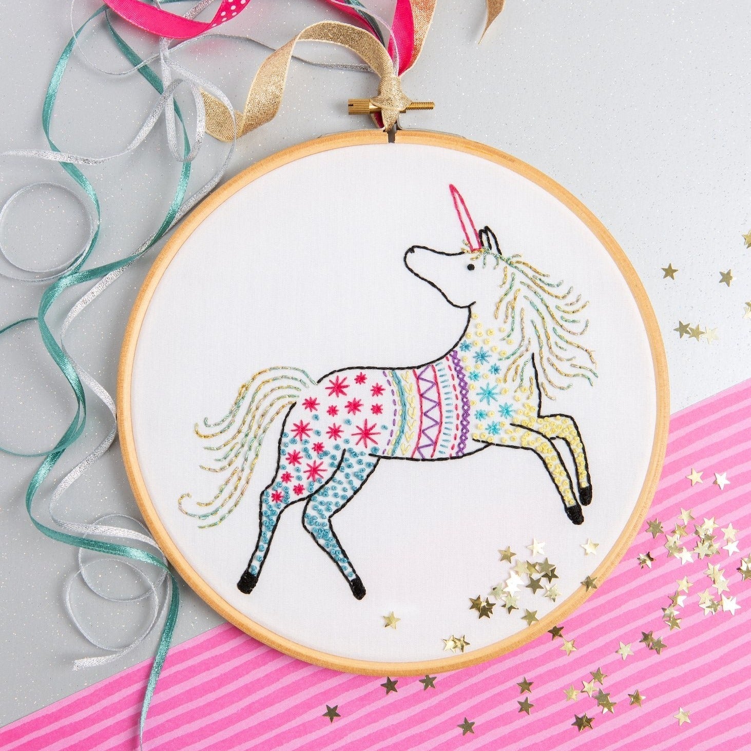 Embroidery hoop with a colorful unicorn design on a pink and gray background