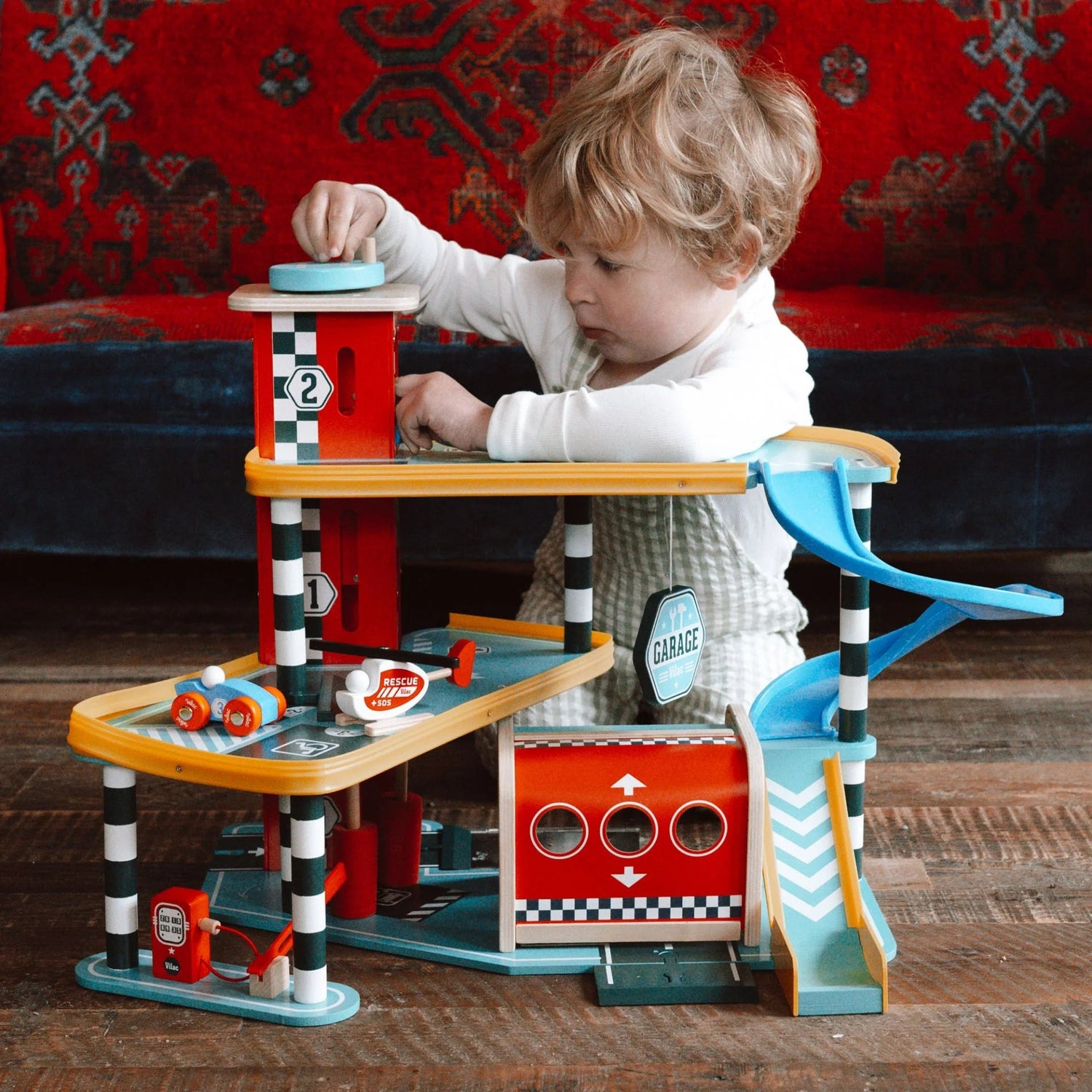 Child playing with a toy garage set on a wooden floor.