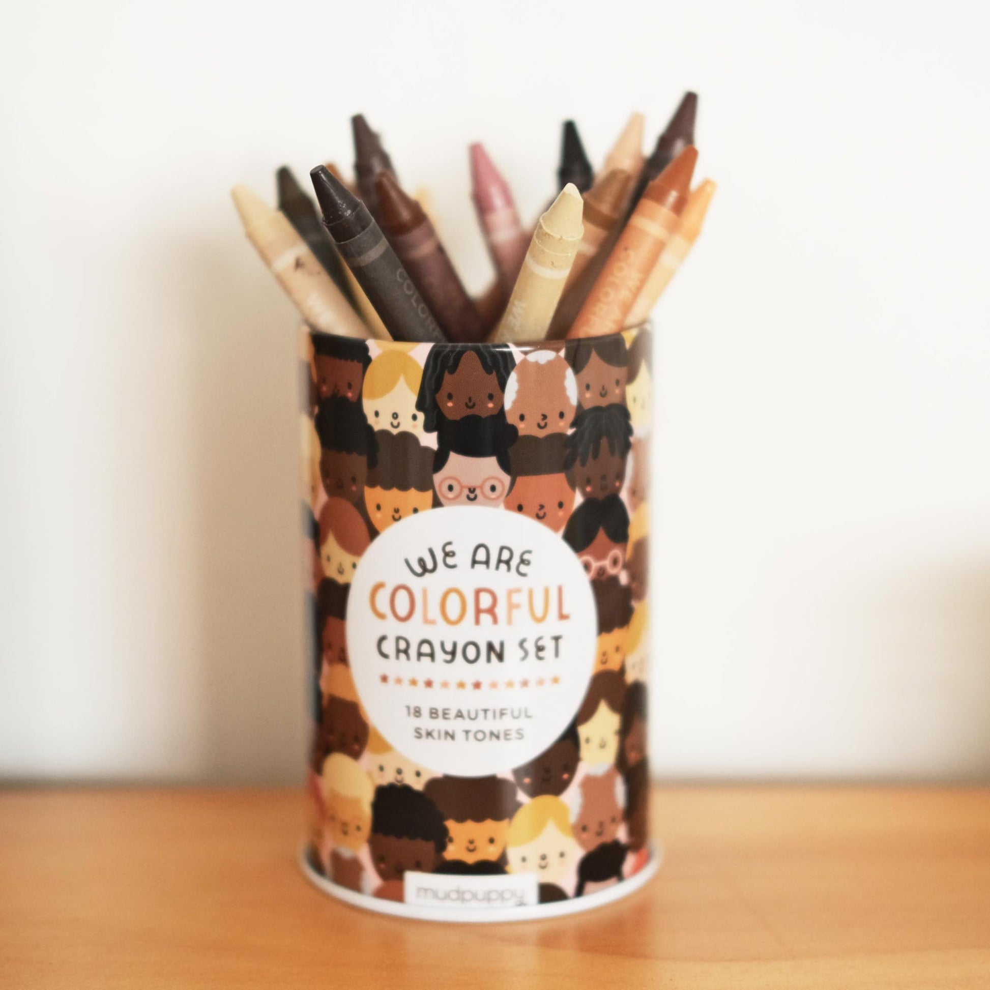 Crayon set with diverse skin tone crayons in a patterned container on a wooden surface.